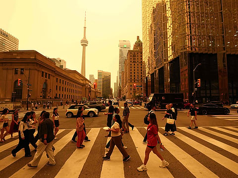 People walk in downtown Toronto, as smoke from forest fires in Northern Ontario causes poor air quality over the city, in Toronto, Ontario, Canada, July 15, 2026.  
