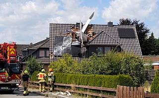 The tail of an airplane protrudes from the roof of a residential building after a crash as firefighters are at work.