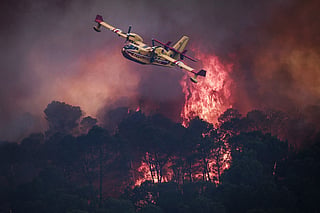 A French Civil Security Canadair CL-415 aircraft flies past flames burning a forest surrounding Cotignac, southeastern Franc during a wildfire.