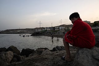 A young man sits on rocks as migrants arrive after swimming to the Spanish enclave of Ceuta in North Africa on July 31, 2026.
