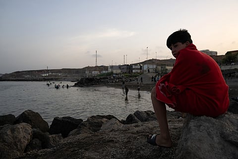 A young man sits on rocks as migrants arrive after swimming to the Spanish enclave of Ceuta in North Africa on July 31, 2026.