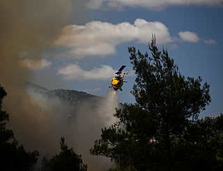 A firefighting helicopter drops water over a smoke-filled forest during a wildfire near Porto Germeno, northwest of Athens, Greece.