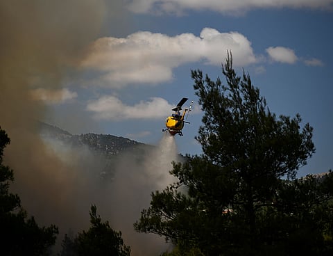 A firefighting helicopter drops water over a smoke-filled forest during a wildfire near Porto Germeno, northwest of Athens, Greece.