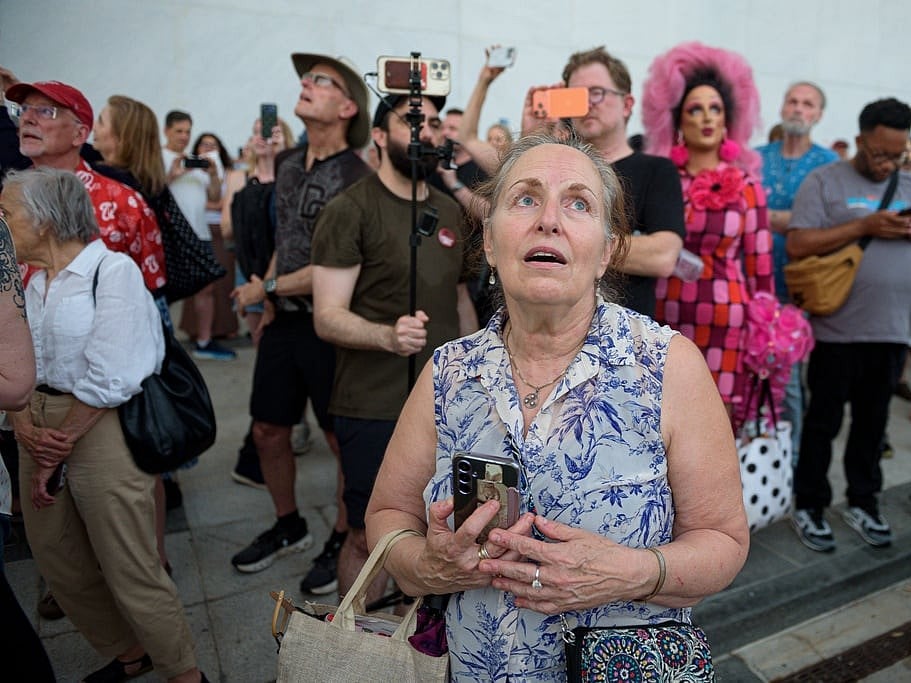 A crowd sings, "God Bless America," as they wait to watch the removal of President Donald Trump's name from the John F. Kennedy Center for the Performing Arts in Washington, June 12, 2026.