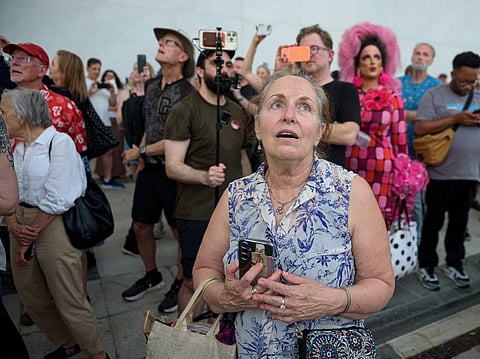 A crowd sings, "God Bless America," as they wait to watch the removal of President Donald Trump's name from the John F. Kennedy Center for the Performing Arts in Washington, June 12, 2026. 