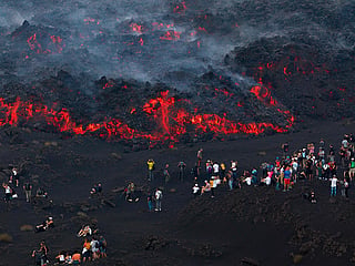 Visitors standing next to lava flowing from Mount Etna volcano during an eruption, in Catania, in the Mediterranean island of Sicily.