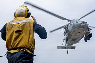 A U.S. Sailor directs an MH-60S Sea Hawk helicopter onto the flight deck of USS Delbert D. Black (DDG 119) while the ship sails in the Arabian Sea enforcing the U.S. blockade against Iran. As of Aug. 30, CentCom forces have redirected 83 commercial vessels, disabled 3 and boarded 2 to ensure compliance with the blockade.