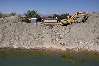 A residence overlooks an open pit dug by illegal miners using an excavator searching for chrome in Bapong, a mining village in North West province, on August 25, 2026.