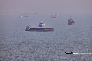 A small boat sails past cargo ships and other commercial vessels anchored in the Strait of Hormuz off Bandar Abbas, Iran.