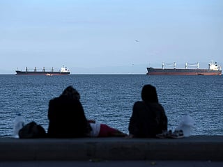 People sit in front of cargo ships anchor in the Marmara Sea await to cross the Bosphorus Straits in Istanbul, Turkey.