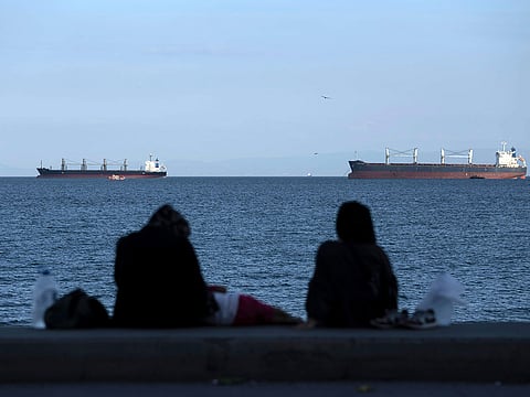 People sit in front of cargo ships anchor in the Marmara Sea await to cross the Bosphorus Straits in Istanbul, Turkey.