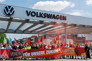 Employees of German car maker Volkswagen (VW) wave flags and display banners as they take part in a rally called by German trade union IG Metall to protest against restructuring and mass job cut plans at the VW plant in Zwickau, eastern Germany on July 9, 2026.
