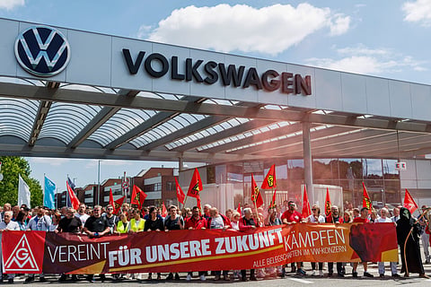 Employees of German car maker Volkswagen (VW) wave flags and display banners as they take part in a rally called by German trade union IG Metall to protest against restructuring and mass job cut plans at the VW plant in Zwickau, eastern Germany on July 9, 2026.