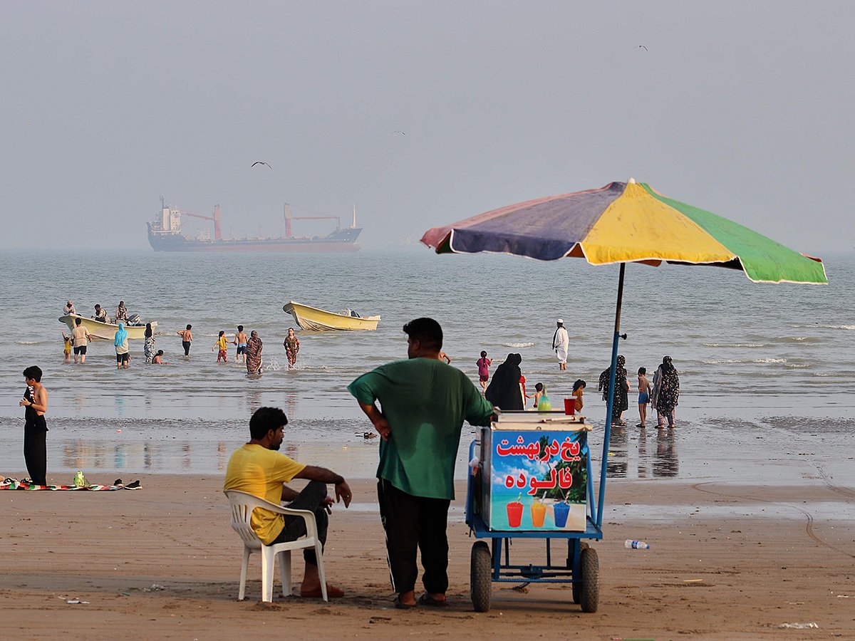 A juice seller serves beachgoers from his cart as commercial vessels sit anchored in the Strait of Hormuz off Bandar Abbas, Iran. 