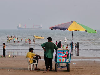 A juice seller serves beachgoers from his cart as commercial vessels sit anchored in the Strait of Hormuz off Bandar Abbas, Iran. 