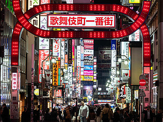 A man is illuminated as he looks up at a large neon sign in the Shinjuku district in Tokyo.