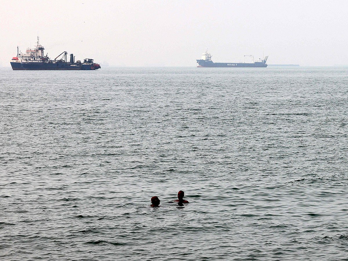 Men bathe in the Gulf waters as vessels in the background transit the Strait of Hormuz off the coast of Iran's southern port city of Bandar Abbas.