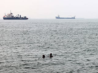 Men bathe in the Gulf waters as vessels in the background transit the Strait of Hormuz off the coast of Iran's southern port city of Bandar Abbas.