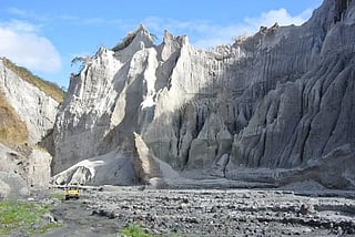 A 4x4 jeepney dwarfed by the lahar cliffs while traversing the landscape created by Mount Pinatubo's eruption.