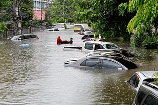 People walk next to cars submerged in flood waters after heavy rain in Bangkok on September 26, 2026.