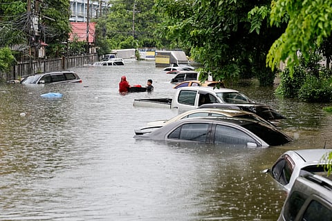 People walk next to cars submerged in flood waters after heavy rain in Bangkok on September 26, 2026.