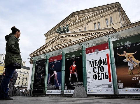 A woman inspects playbills in front of the Bolshoi Theatre in Moscow on September 24, 2026, including "Mefistofele" opera (2nd R) for the first time to be conducted by maestro Valery Gergiev.