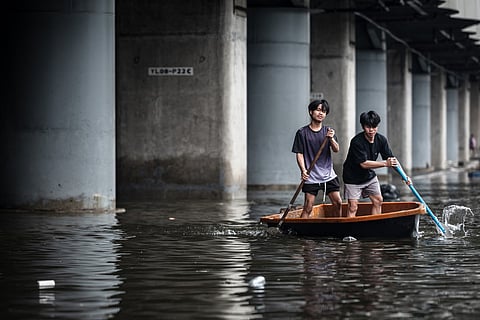People paddle a plastic boat along a flooded road in the Bang Kapi district of Bangkok on September 27, 2026.