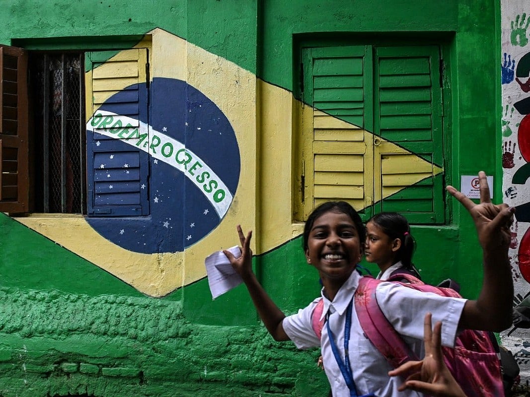 Students react as they walk past a graffiti featuring the Brazilian national flag ahead of a FIFA international friendly football match between India and Brazil in Kolkata on October 1, 2026.