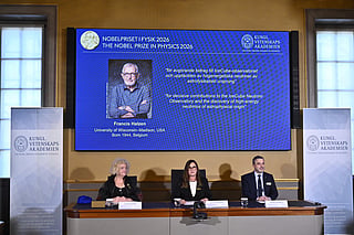 Eva Olsson, Ellen Moons, and Mark Pearce sit in front of a screen displaying Francis Halzen as the recipient of the 2026 Nobel Prize in Physics during a press conference at the Royal Swedish Academy of Sciences in Stockholm, Sweden, on October 6, 2026.
