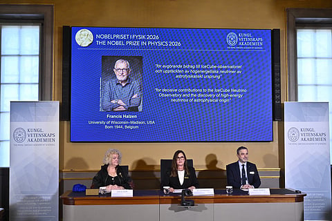 Eva Olsson, Ellen Moons, and Mark Pearce sit in front of a screen displaying Francis Halzen as the recipient of the 2026 Nobel Prize in Physics during a press conference at the Royal Swedish Academy of Sciences in Stockholm, Sweden, on October 6, 2026.