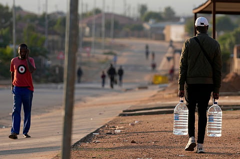 FILE - A man carrying water bottles walks along a dusty street in Hamanskraal, Pretoria, South Africa, Friday, May 26, 2023. (AP Photo/Themba Hadebe, File)