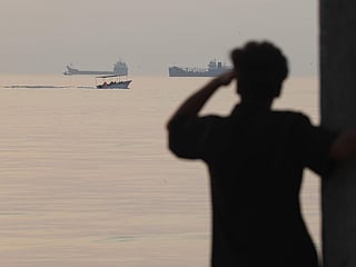 A man looks out over the water as a small boat passes cargo ships anchored in the Strait of Hormuz off Bandar Abbas, Iran, early Saturday, October 24, 2026.