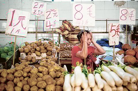 A vegetable vendor is seen among price labels at a vegetable market in Beijing. Food prices fell in December, with vegetable price gains slowing. 