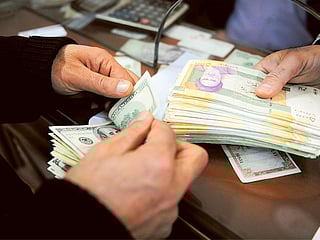 A currency trader prepares to exchange Iranian rial notes, right, for US dollar notes, in Tehran. 