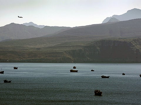 A plane flies over the mountains, south of the Strait of Hormuz, as trading dhows and ships are docked on the Arabian Gulf waters near the town of Khasab, in Oman.