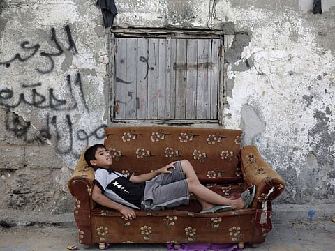A boy rests on an old couch in front of a dilapidated house in Gaza where more than 40 per cent of people remain below the poverty line