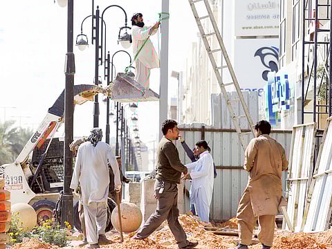 Labourers work to remove a pole outside a residential building in Riyadh. Fines linked to non-compliance in protection, safety, and occupational health have been revised.