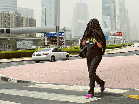 A resident protect  herself from the sun on a hot and humid afternoon in Dubai. 