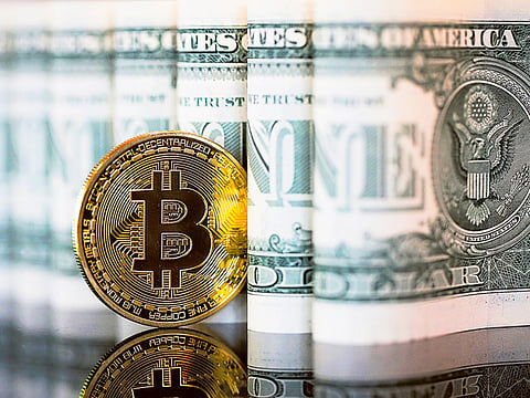 A bitcoin token stands next to a collection of US one dollar bills in this arranged photograph in London.