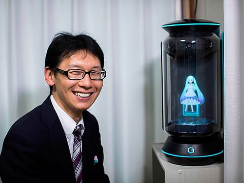 Japanese Akihiko Kondo poses next to a hologram of Japanese virtual reality singer Hatsune Miku at his apartment in Tokyo, 