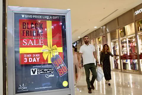 Customers at a mall in Dubai pass a sign advertising a Black Friday sale by an outlet. Both online and physical stores are running their year-end super sales.