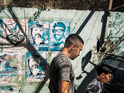 Ebrahim Al Qasim, 22, walks past a poster of the late Palestinian leader Yasser Arafat. Like many young people in the Bourj El Barajneh refugee camp, he is unemployed.