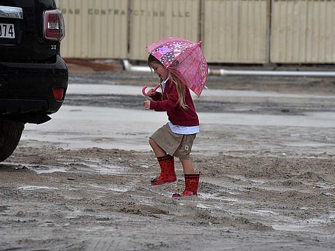 A child walks under the rain on her the way to school at Dubai Sports City. 