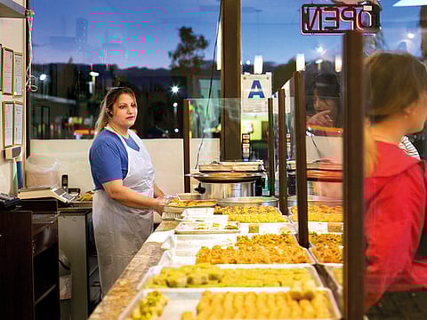 Manar Al Najjar working the front counter at her family’s sweet shop. Her husband does the baking in the back.