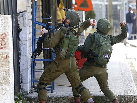 Israeli soldiers throw sound bombs as they clash with Palestinians during a search for suspects of a shooting attack in the West Bank City of Ramallah