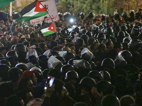 Jordanian protesters wave their national flag as the are confronted by riot police in the capital Amman during a demonstration against the government's decision to raise the income tax.
