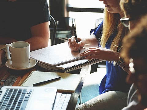 A multi-ethnic group of business people are indoors in an office boardroom.