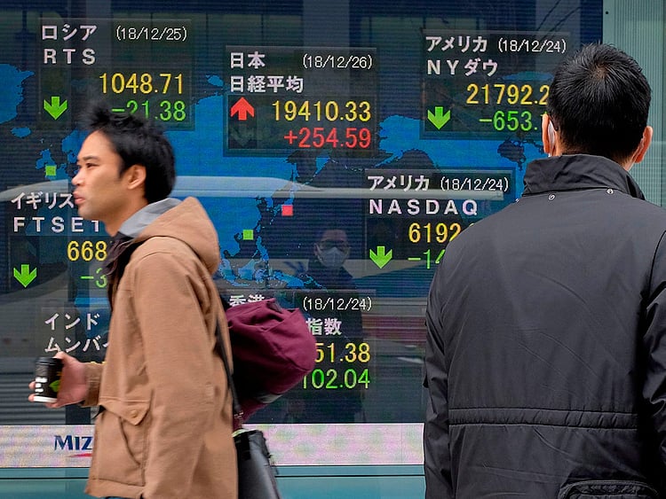 Pedestrians walk past a stock indicator