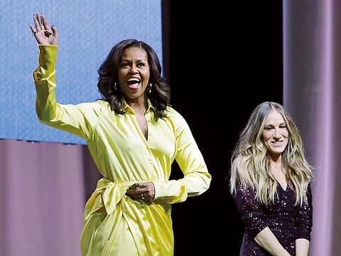 Former first lady Michelle Obama, left, waves to a crowd as Sarah Jessica Parker watches during an appearance for her book, "Becoming: An Intimate Conversation with Michelle Obama" at Barclays Center Wednesday, Dec. 19, 2018, in New York.