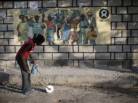 A boy playing with a homemade toy walks past an Oxfam sign in Corail, a camp for displaced people of the earthquake of 2010, on the outskirts of Port-au-Prince, Haiti, February 17, 2018. 